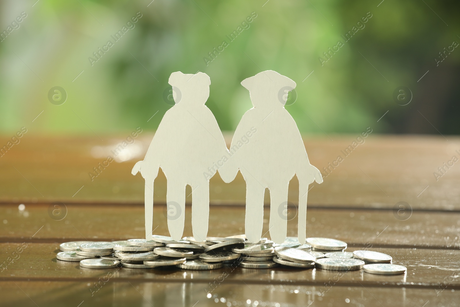 Photo of Pension savings. Figure of senior couple and coins on wooden table outdoors