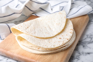Photo of Wooden board with corn tortillas on marble table. Unleavened bread