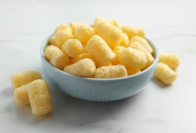 Photo of Bowl of delicious crispy corn sticks on white marble table