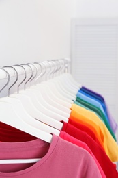 Photo of Rack with bright clothes in room. Rainbow colors