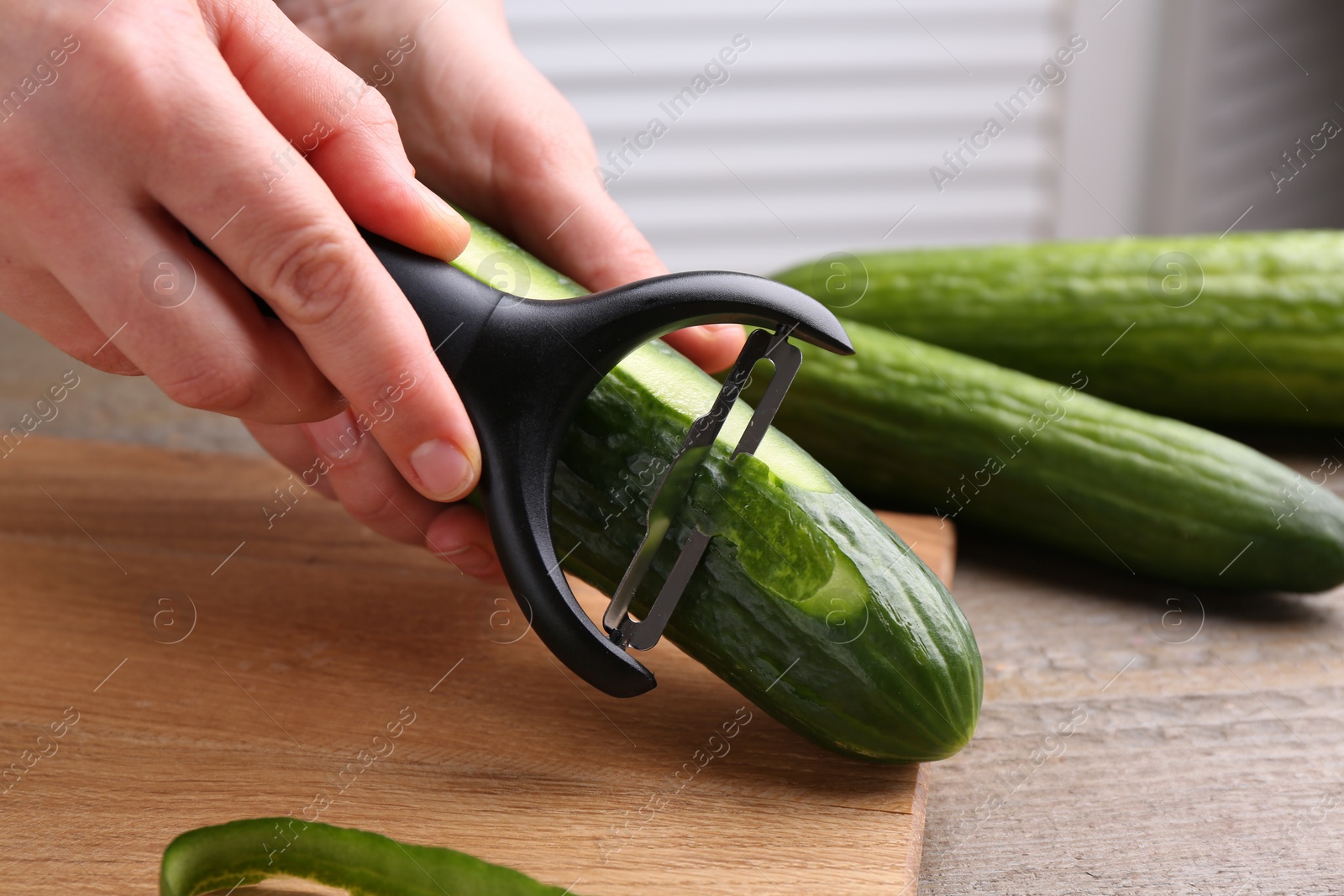 Photo of Woman peeling cucumber at wooden table indoors, closeup