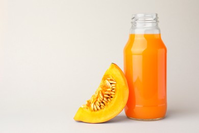 Photo of Tasty pumpkin juice in glass bottle and cut pumpkin on light background. Space for text