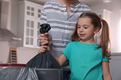 Photo of Little girl taking garbage bag out of bin in kitchen. Separate waste collection