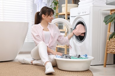 Young housewife putting laundry into washing machine at home