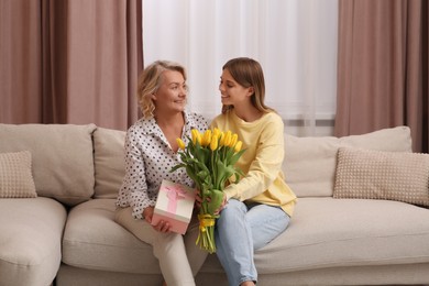 Photo of Young daughter congratulating her mom with flowers and gift at home. Happy Mother's Day