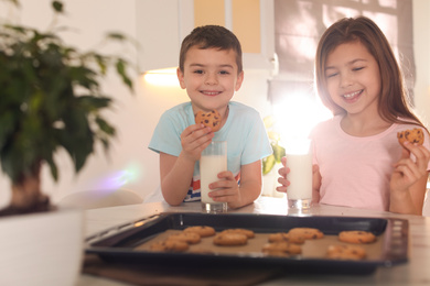 Photo of Cute little children eating cookies with milk in kitchen. Cooking pastry