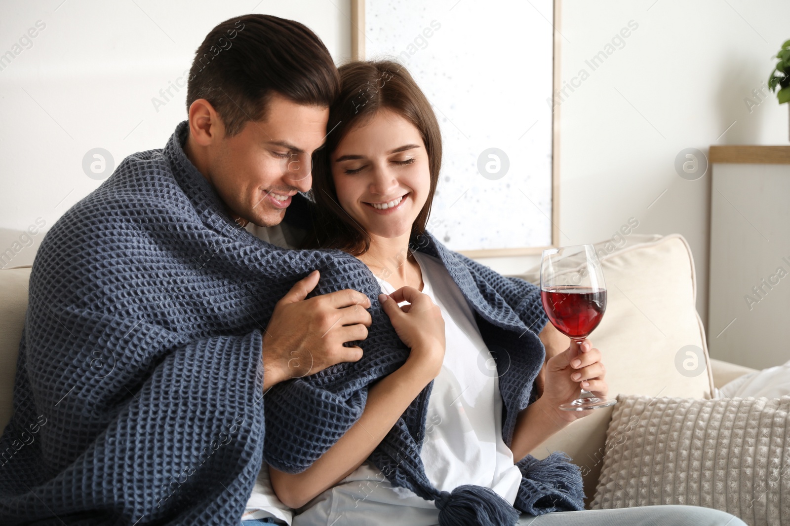 Photo of Happy couple covered with warm dark blue plaid on sofa at home