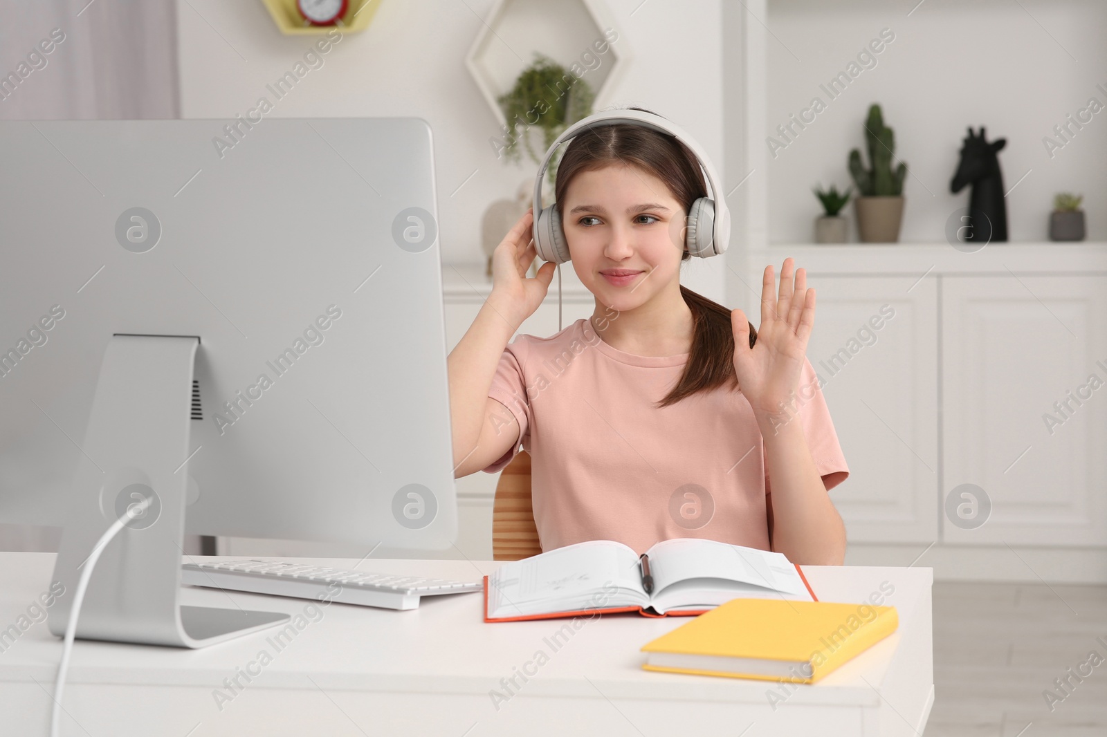 Photo of Cute girl using computer and headphones at desk in room. Home workplace