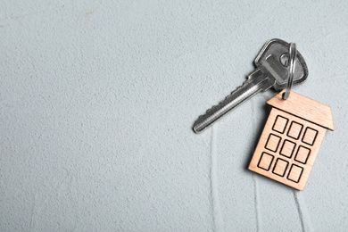 Photo of Key with trinket in shape of house on grey stone background, top view and space for text. Real estate agent services