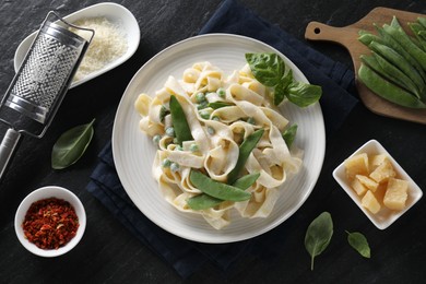 Photo of Delicious pasta with green peas and ingredients on black table, flat lay