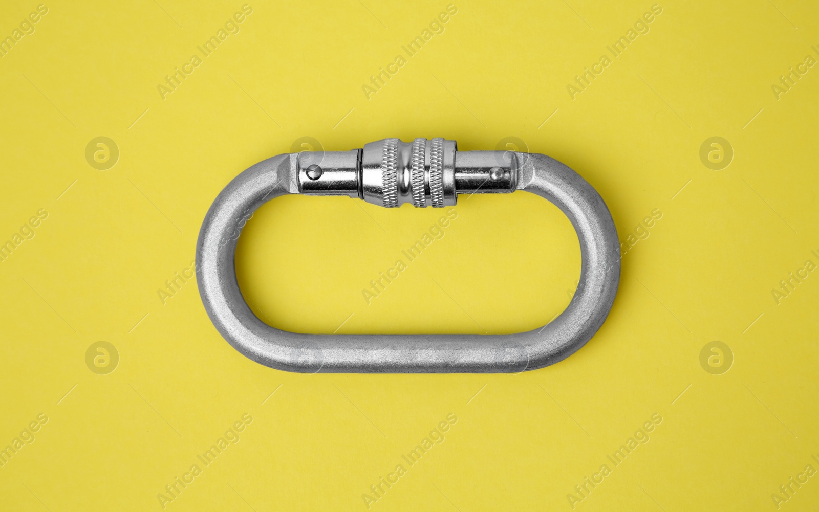 Photo of One metal carabiner on yellow background, top view