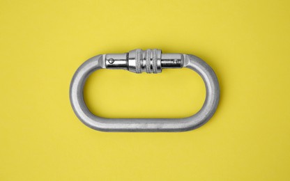 Photo of One metal carabiner on yellow background, top view