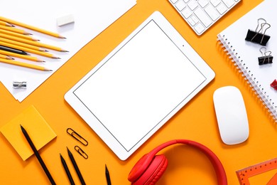 Modern tablet, keyboard and stationery on orange background, flat lay. Space for text