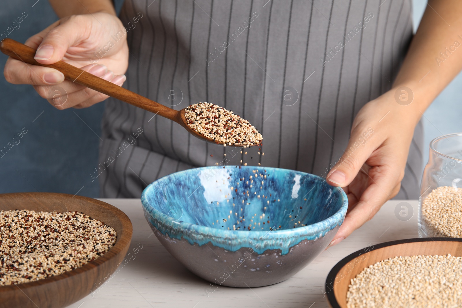 Photo of Woman pouring mixed quinoa seeds into bowl at table, closeup