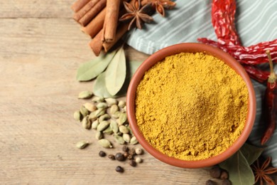 Photo of Curry powder in bowl and other spices on wooden table, flat lay. Space for text