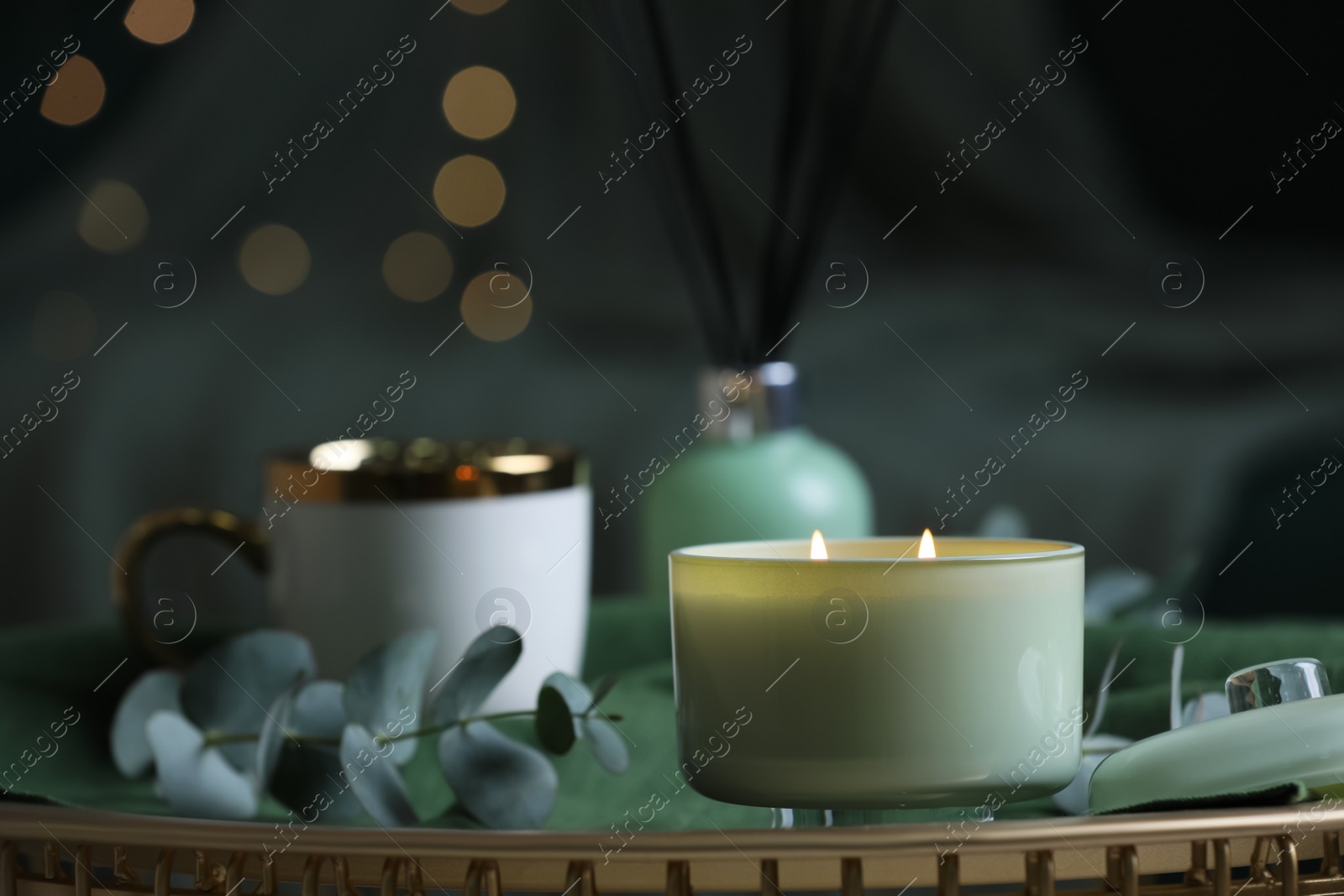 Photo of Beautiful burning candle, cup and eucalyptus branch on table indoors. Bokeh effect