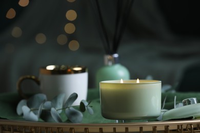 Beautiful burning candle, cup and eucalyptus branch on table indoors. Bokeh effect