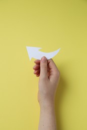 Photo of Woman holding curved paper arrow on yellow background, top view