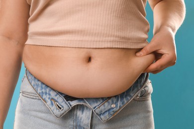 Woman touching belly fat on light blue background, closeup. Overweight problem