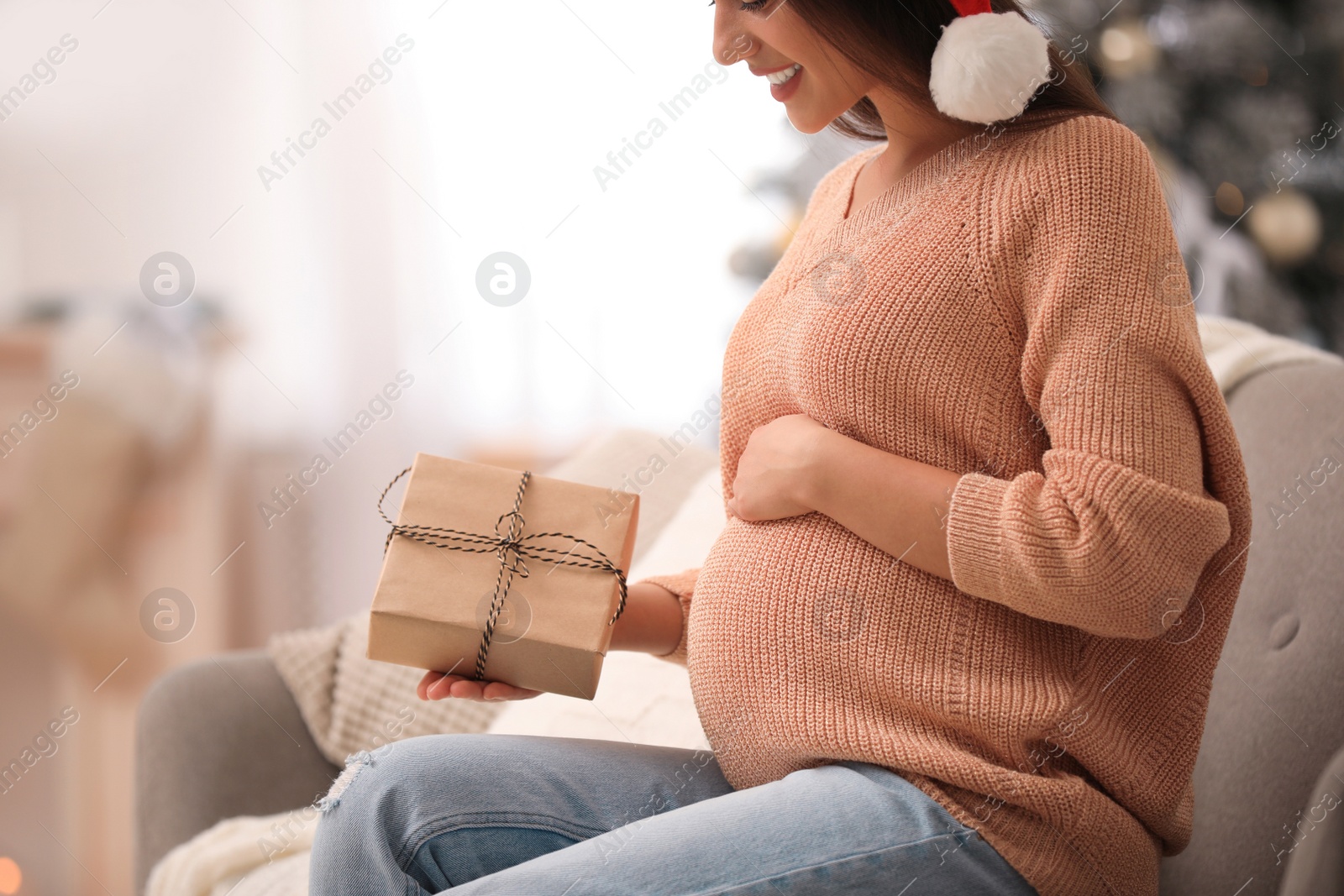 Photo of Happy pregnant woman with Christmas gift box at home, closeup. Expecting baby