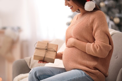 Happy pregnant woman with Christmas gift box at home, closeup. Expecting baby