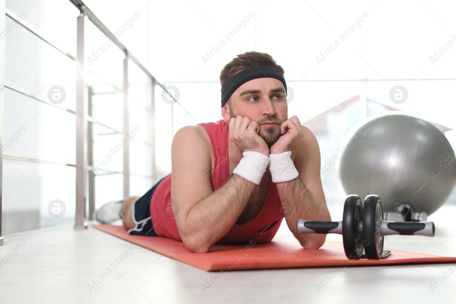 Photo of Lazy young man with abs roller lying on yoga mat indoors