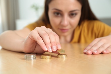 Photo of Young woman stacking coins at table, focus on hand