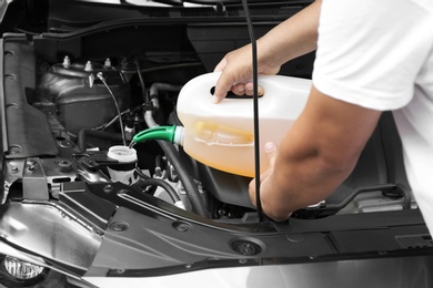 Photo of Man pouring liquid from plastic canister into car washer fluid reservoir, closeup