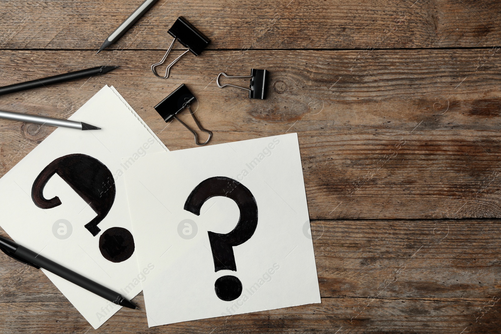 Photo of Sheets of paper with question marks and stationery on wooden table, flat lay