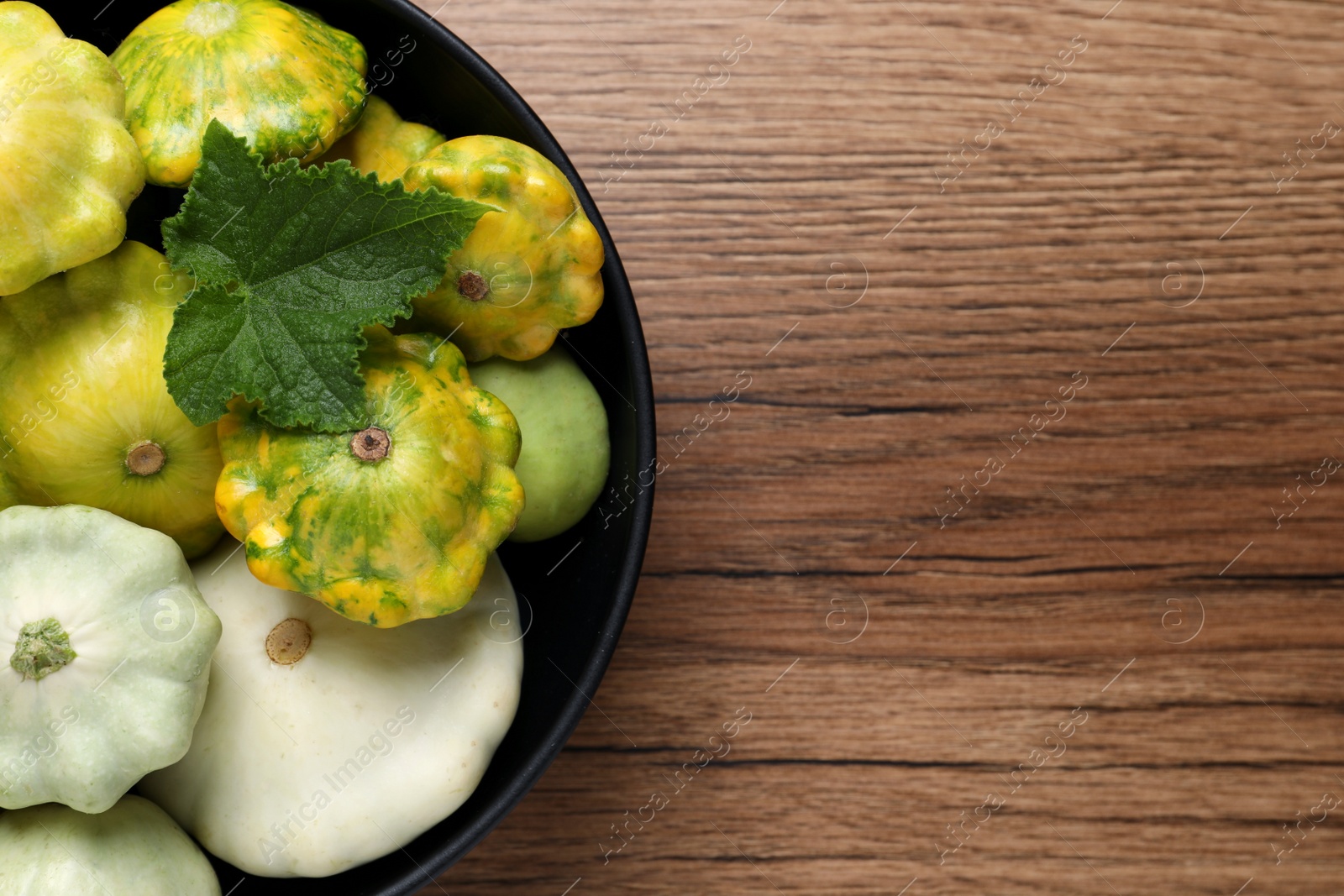 Photo of Fresh ripe pattypan squashes in bowl on wooden table, top view. Space for text