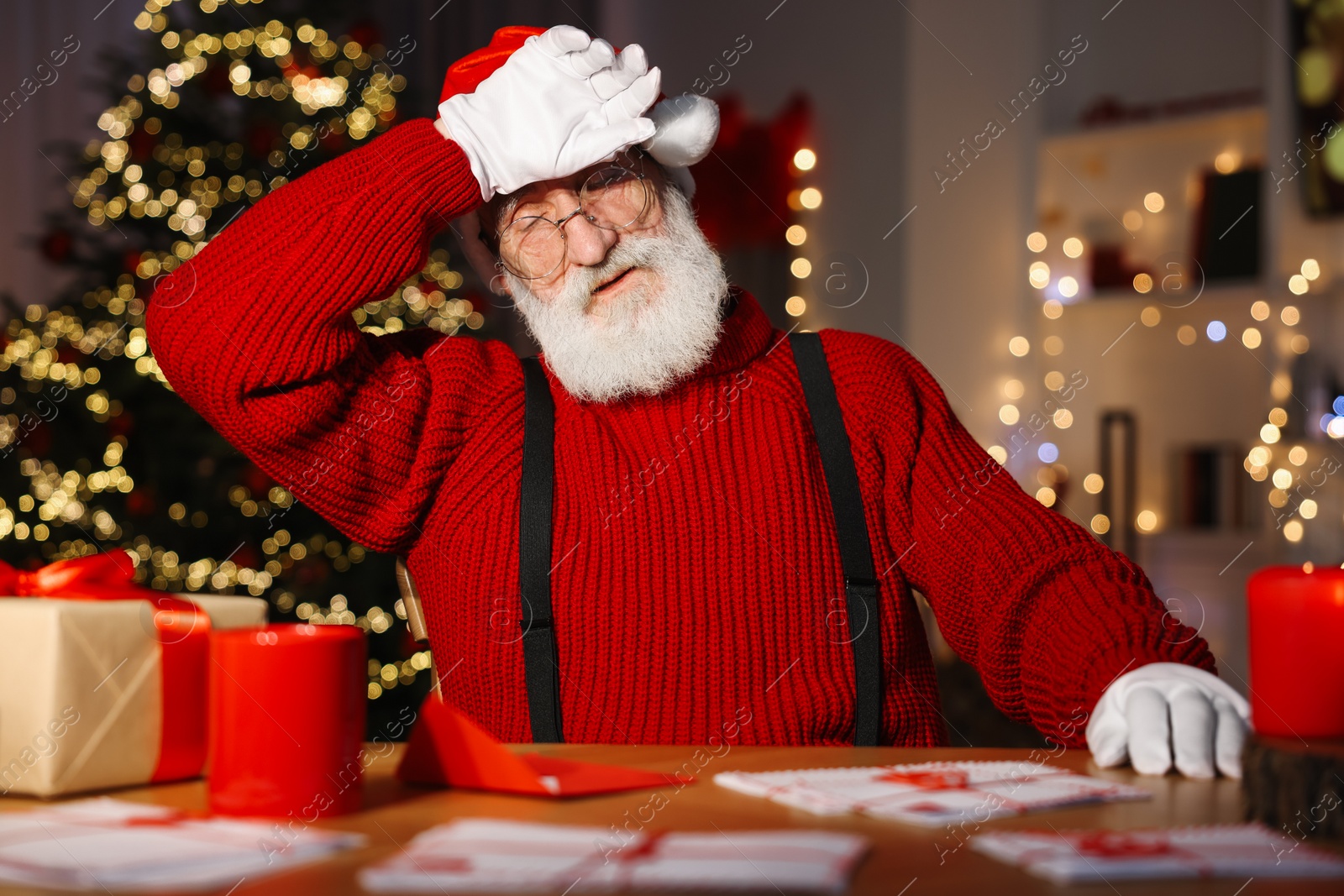 Photo of Tired Santa Claus at his workplace. Letters and gift box on table in room with Christmas tree