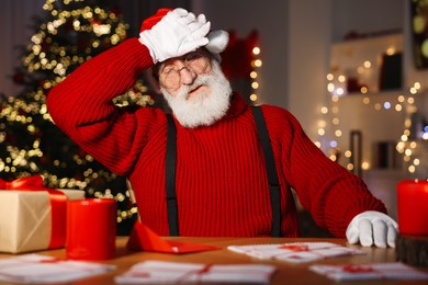 Tired Santa Claus at his workplace. Letters and gift box on table in room with Christmas tree