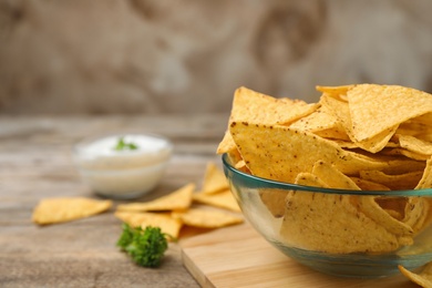 Bowl of Mexican nacho chips on wooden table. Space for text