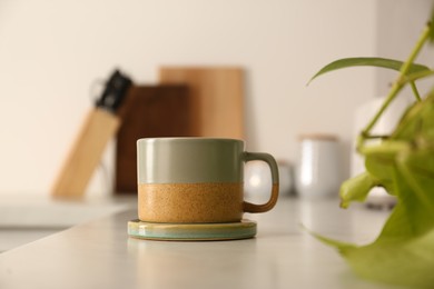 One ceramic mug with coaster on light countertop in kitchen