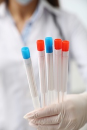 Doctor holding tubes with cotton swabs for DNA test in clinic, closeup