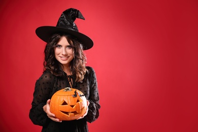 Photo of Beautiful woman in witch costume with jack o'lantern on red background, space for text. Halloween party