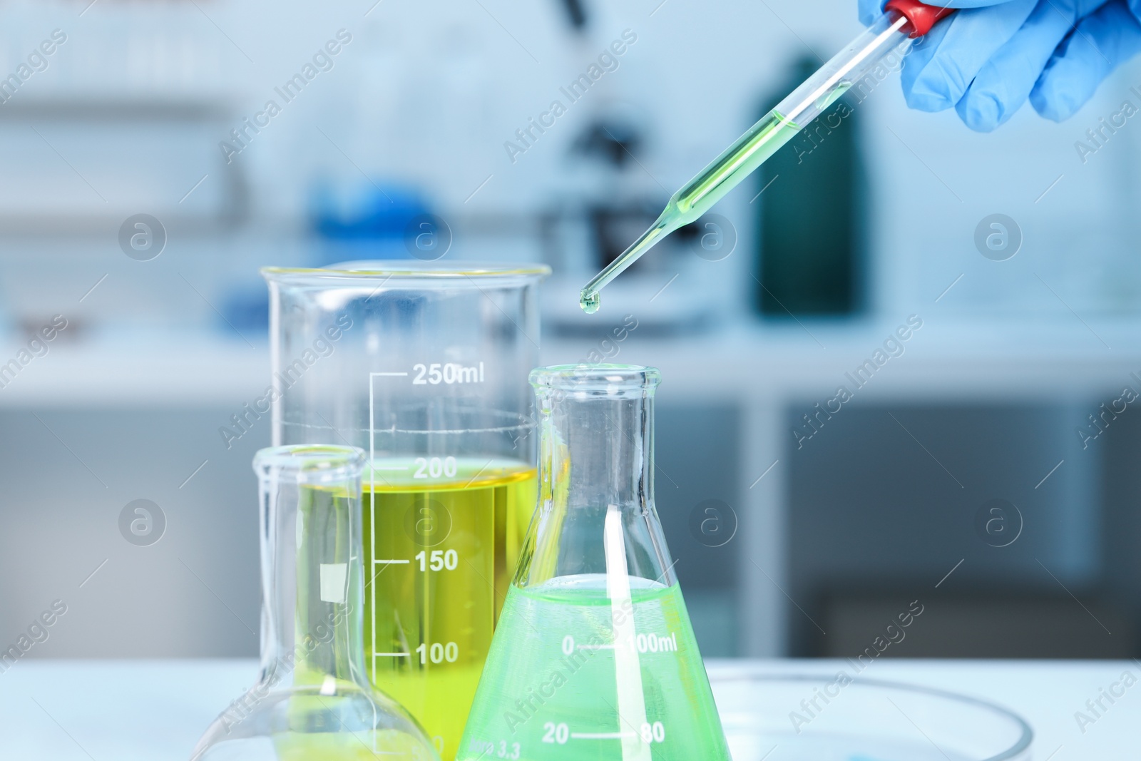 Photo of Laboratory analysis. Woman dripping liquid into flask at white table indoors, closeup