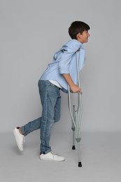Photo of Teenage boy with injured leg using crutches on grey background