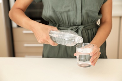 Photo of Woman pouring water from bottle into glass in kitchen, closeup