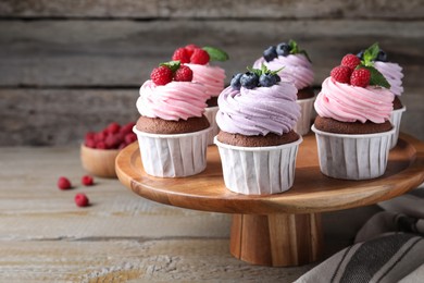 Photo of Dessert stand with sweet cupcakes on wooden table. Space for text