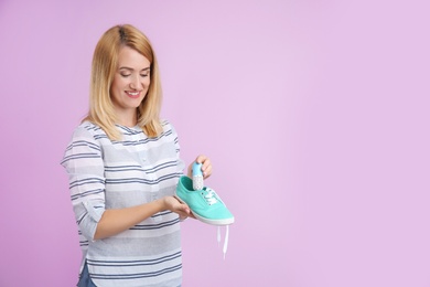 Young woman putting capsule air freshener in shoe on color background