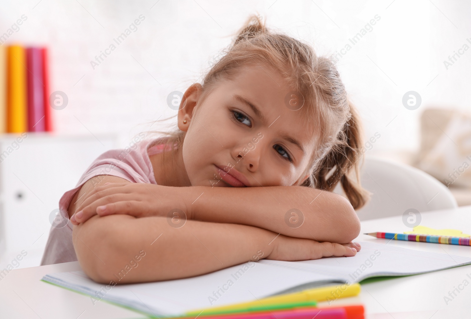 Photo of Tired little girl at table. Doing homework