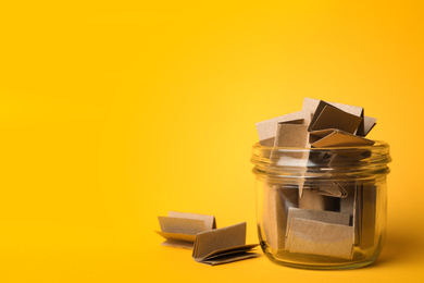 Photo of Glass jar full of brown paper sheets on yellow background, space for text