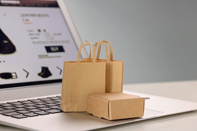 Photo of Mini shopping bags and box on laptop against light grey background, closeup. Online store