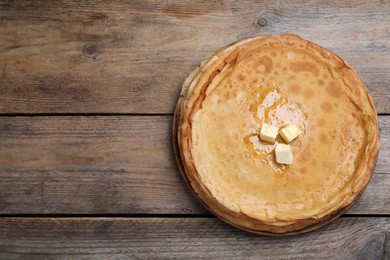 Stack of delicious crepes with melting butter on wooden table, top view. Space for text