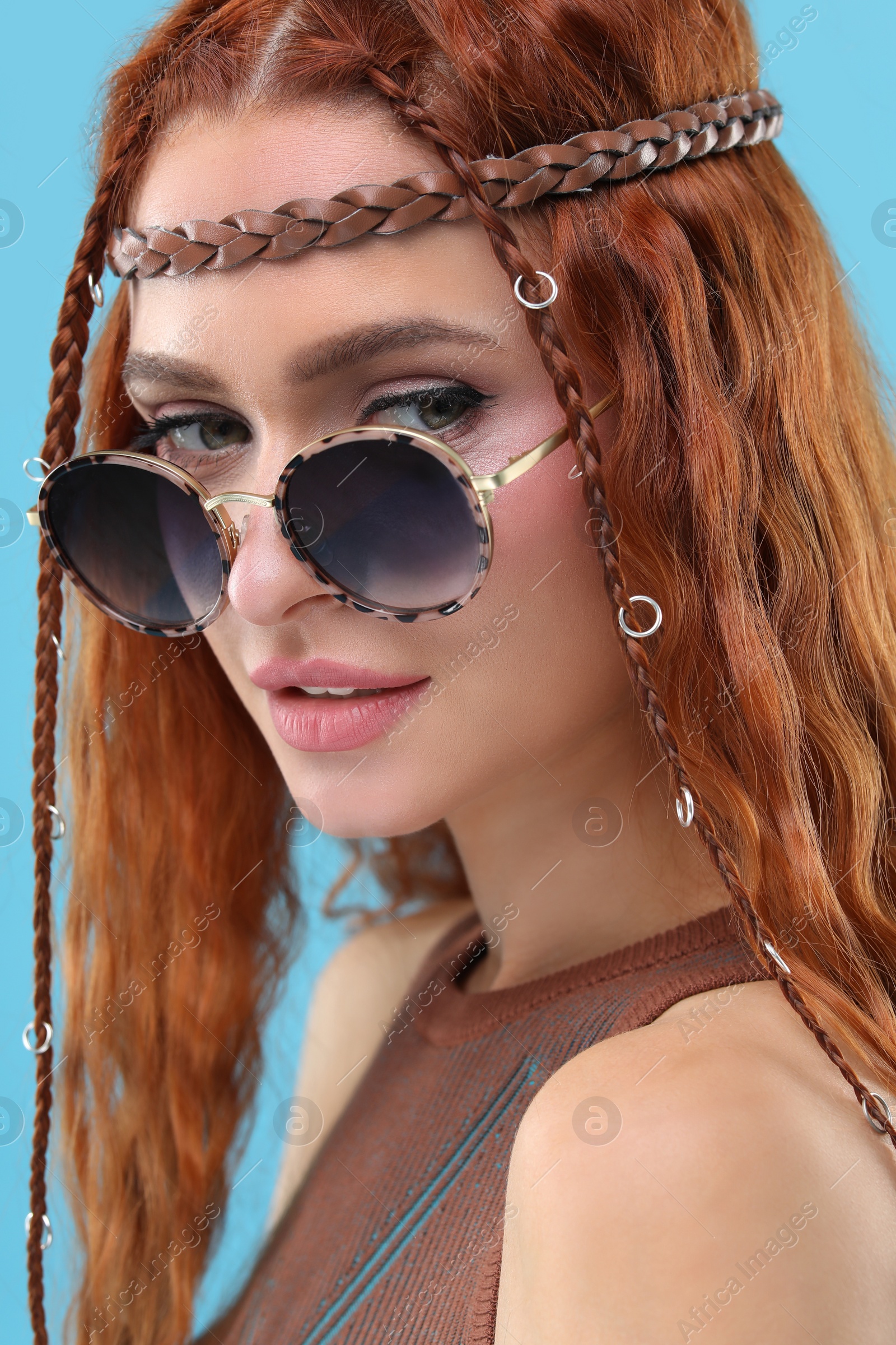 Photo of Stylish young hippie woman in sunglasses on light blue background, closeup