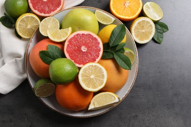 Photo of Different fresh citrus fruits and leaves on grey textured table, flat lay