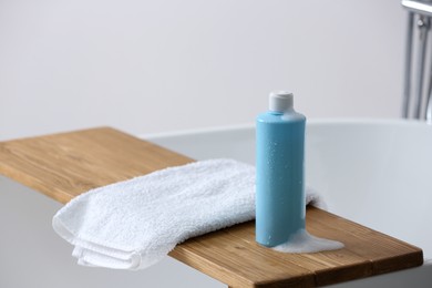 Photo of Bottle of bubble bath with foam and towel on tub in bathroom, space for text