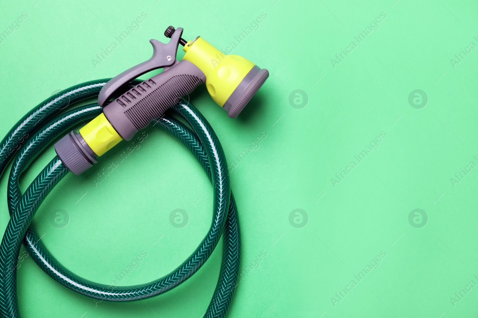 Photo of Watering hose with sprinkler on green background, top view. Space for text