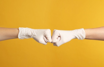 Photo of Doctors in medical gloves making fist bump on yellow background, closeup